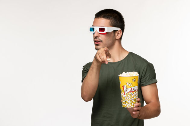 观看正面图身穿绿色t恤的年轻男性手持爆米花in-d太阳镜在白墙上看电影孤独电影院男性电影电影院肖像电影