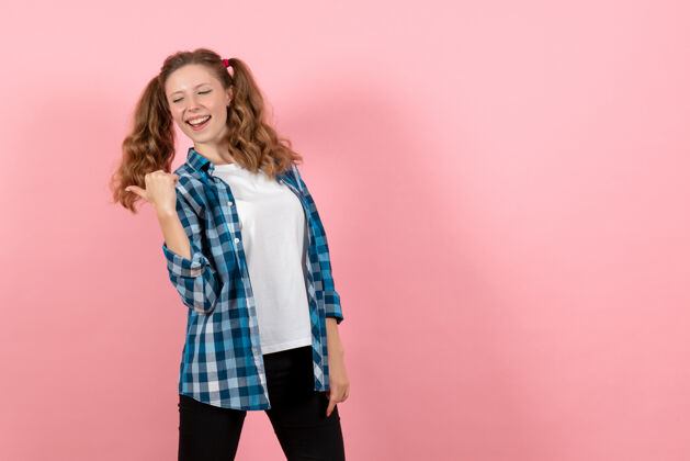 年轻女性正面图身着蓝色格子衬衫的年轻女性在粉色背景上摆姿势儿童青少年情感模特时尚女性色彩人格子肖像