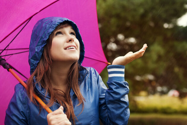护理穿着雨衣 带着雨伞的漂亮年轻女子正在检查是否下雨站可爱候选人