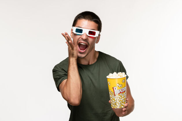 爆米花正面图身穿绿色t恤的年轻男性手持爆米花包戴着d墨镜在浅白墙上拍摄电影孤独电影院男性电影看法包装电影