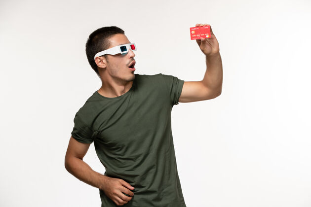 电影正面图身穿绿色t恤的年轻男子戴着d墨镜拿着银行卡在浅白墙上拍摄电影《孤独电影院》银行观点男人