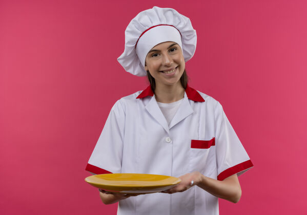持有身着厨师制服 面带微笑的白人厨师女孩拿着盘子 看着粉色的相机 还有复印空间空间烹饪制服