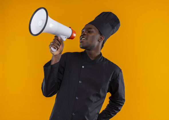 通过穿着厨师制服的年轻的美国黑人厨师在橘子色的大喇叭里大声喊叫 还有复印空间恼怒年轻非裔美国人