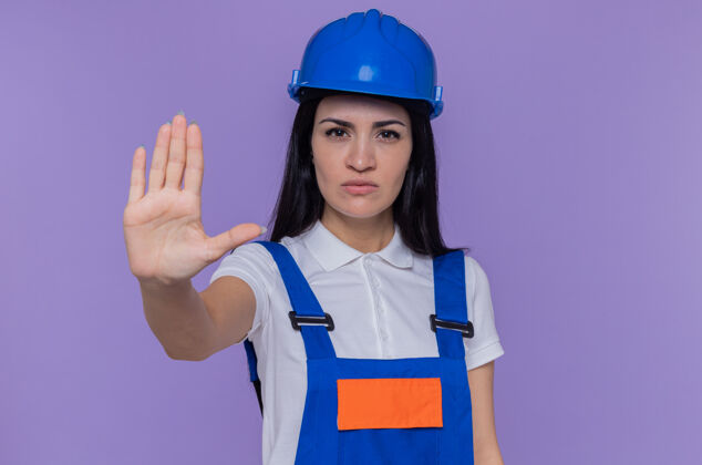 站立年轻的建筑女工穿着建筑制服 戴着安全帽看着摄像机制造建设者停止