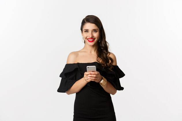 美丽网上购物概念穿黑衣服的年轻女子 看短信 用手机 微笑着 站在白色的背景下模型年轻表情