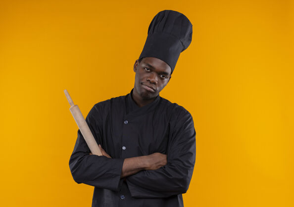 交叉年轻恼怒的非洲裔美国厨师身着厨师制服 双手交叉拿着擀面杖放在橘子上 留有复印空间烹饪年轻滚动