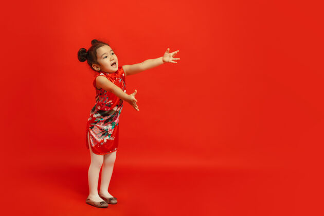 欢呼给朋友和家人一个拥抱…亚洲可爱的小女孩在传统服装隔离在红墙上庆祝 人类的情感 节日的概念复制空间旗袍肖像美丽