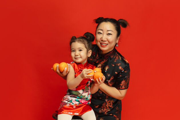 旗袍拥抱 微笑 抱着乡巴佬穿着传统服装的红墙上的亚洲母女肖像庆祝 人类情感 节日复制空间普通话服装祝福