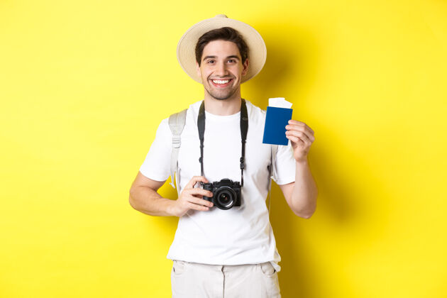 时尚旅游 度假和旅游理念微笑的男人拿着相机 出示护照和门票 站在黄色背景上男人假日帽子