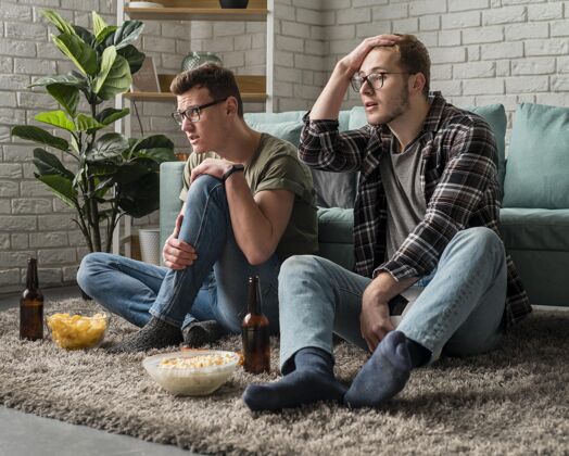 男男性朋友一起看电视体育节目 一边吃零食和啤酒看一起哥们