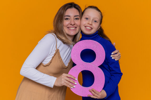 欢呼慈爱的母女抱着纸板做的8号 站在橘红色的墙上 面带微笑 兴高采烈地庆祝国际妇女节纸板制造八