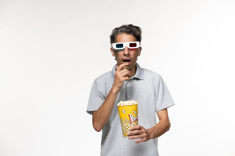 遥控正面图年轻男性手持爆米花包戴着d墨镜在白色表面电影孤独包装