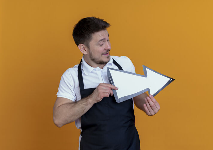 人围裙上的理发师手里拿着白色的箭 站在橙色的墙上微笑着看着它箭理发师拿着