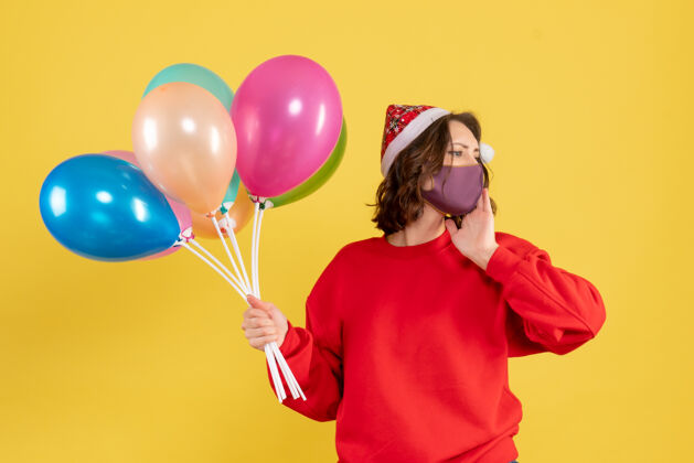 正面正面图：戴着黄色面具手持气球的年轻女子面具外科面具派对