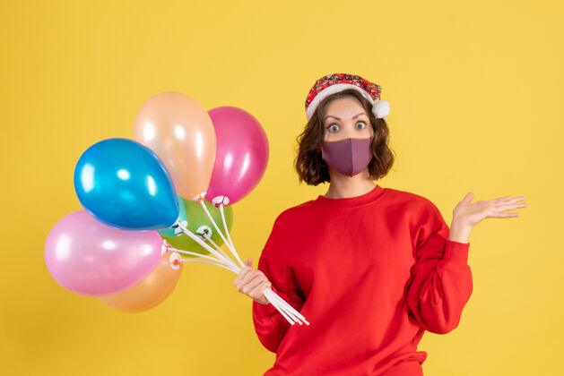 外科面具正面图：戴着面具手持气球的年轻女子在一个黄色派对上庆祝新年色彩的情感女子庆祝女人气球
