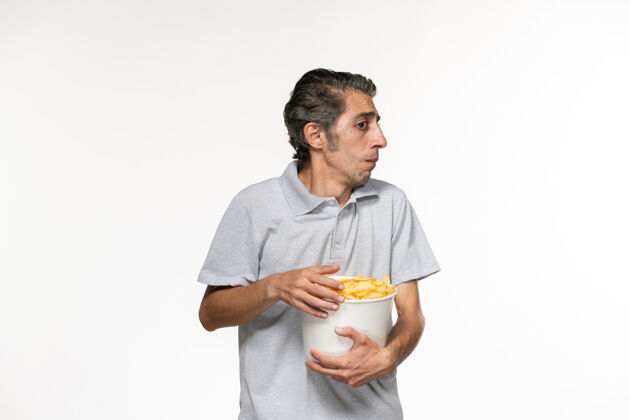 土豆正面图：年轻男性在白色表面上吃薯片看电影孤独前方观看