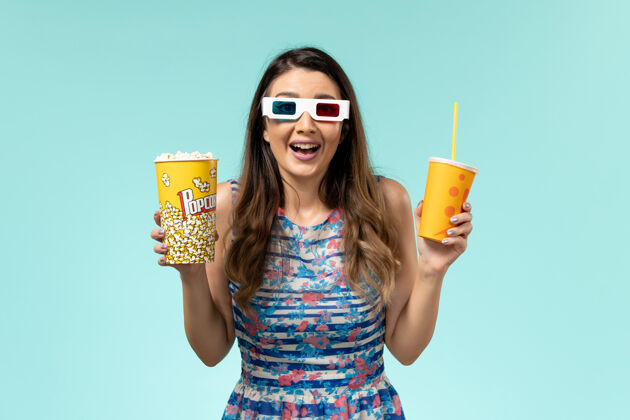 太阳镜前视图年轻女性手持爆米花饮料在d太阳镜浅蓝色表面电影院前面爆米花