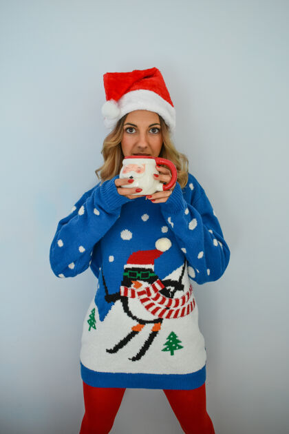 衣服一个穿着圣诞礼服 戴着圣诞帽 手里拿着圣诞杯子的年轻漂亮女士的垂直镜头漂亮茶季节