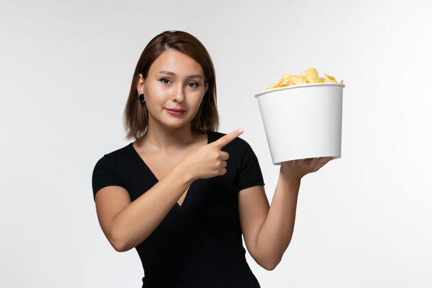 漂亮正面图：身穿黑色衬衫的年轻女性在白色表面上拿着薯片家庭主妇电影院电影