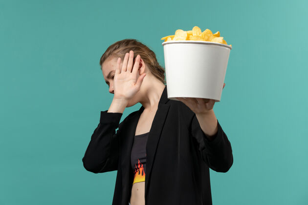 年轻女性正面图：年轻女性在蓝色桌子上吃薯片看电影观看公司剧院