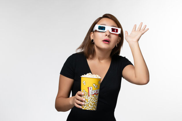 抱正面图年轻女性戴着d型太阳镜拿着爆米花 在白色表面看电影电影前面太阳镜