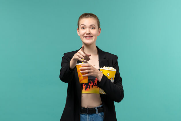 漂亮正面图年轻女性拿着爆米花拿着饮料 在蓝色的桌子上看电影年轻女性抱着爆米花