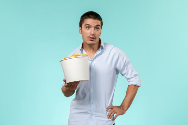 抱着正面图：年轻的男性拿着蓝面薯片的篮子前面土豆电影院