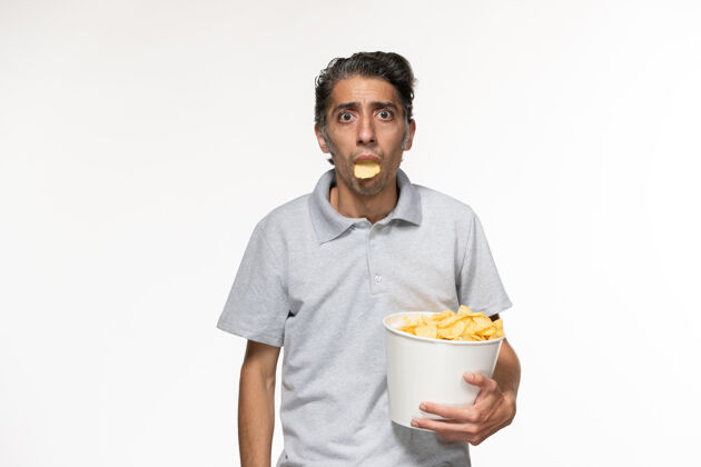看正面图：年轻男性手持薯片 在白色表面上看电影孤独年轻的男性男