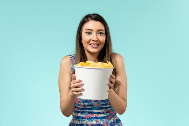 年轻的女性正面图：年轻的女性拿着篮子和薯片 在蓝色的桌子上看电影电影院剧院篮子