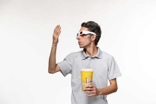 男正面图：年轻的男性手拿着爆米花包 戴着d型太阳镜 坐在一张白色的桌子上爆米花手持电影院