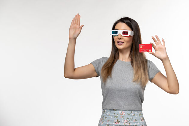 美丽正面图：戴着d型太阳镜手持红色银行卡的年轻女性在白色表面挥舞着她的手前面手银行