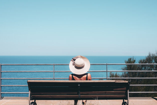 太阳帽戴着白色草帽的女人坐在长凳上看海帽子家具长凳