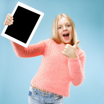 小蓝色画室背景上有一个有趣的小女孩拿着平板电脑她拿着东西指着屏幕童年惊喜欢呼