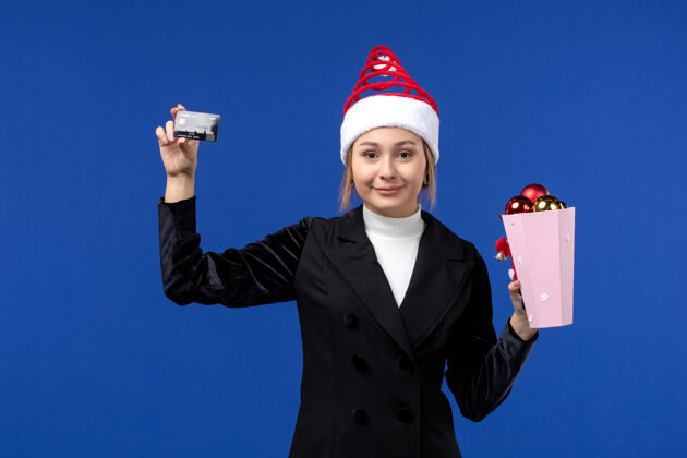 玩具前视图：带着圣诞树玩具和银行卡的年轻女士在蓝色的墙壁上感慨新年假期银行肖像圣诞节