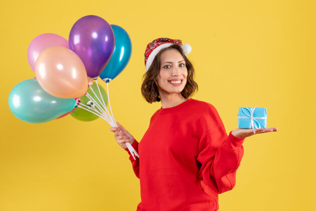 颜色正面图年轻女子拿着气球和小礼物过黄色圣诞佳节新年彩女感慨礼物情感女人