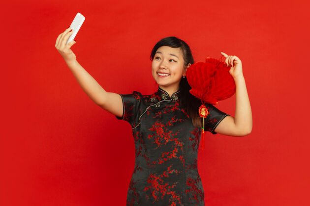 节日年轻的亚洲女人在自拍 中国灯笼被隔离在红墙上庆祝服饰青少年