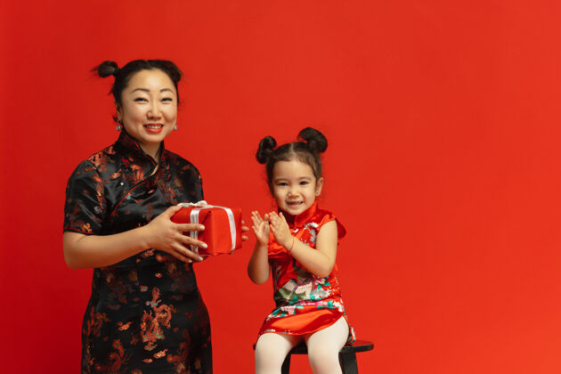 中国新年穿着传统服装的亚洲母女肖像被隔离在红墙上中国服装女性