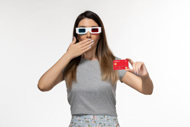 前面正面图年轻女性手持红色银行卡戴着d墨镜在浅白的表面美丽遥远太阳镜
