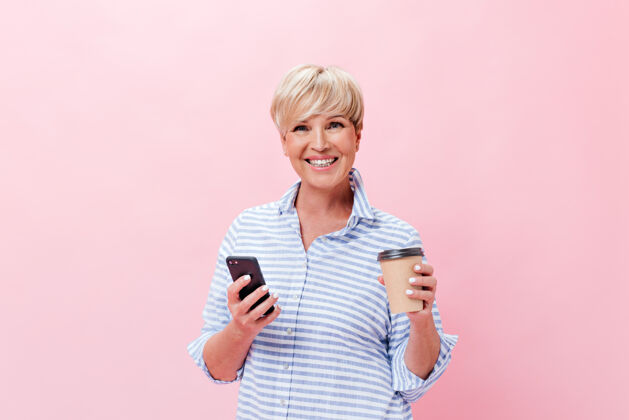 头发心情好的女士拿着粉色背景的咖啡杯和手机摆姿势老年人成年人朋友