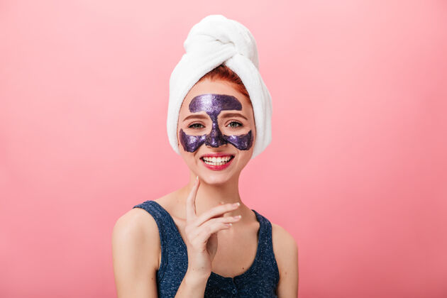 皮肤粉色背景下 迷人的女人戴着面具笑着摄影棚拍摄的幸福女孩头上戴着毛巾做水疗健康皮肤护理面膜