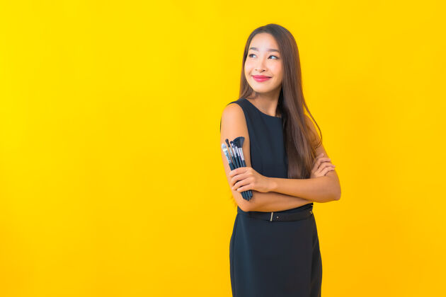 相机在黄色背景上用化妆刷描绘美丽的亚洲女商人在线女孩博客
