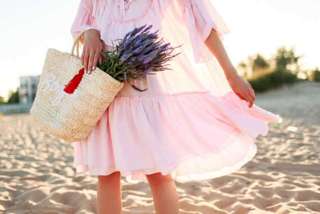 乡村浪漫的金发女郎 穿着可爱的粉色连衣裙 在沙滩上跳舞 手捧草包和薰衣草花束 自由和自然的概念自由自然海洋