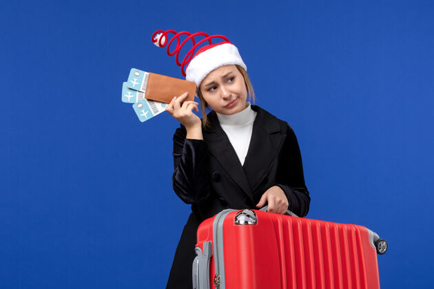 工作正面图年轻的女性拿着包和机票在蓝墙飞机度假旅行商人爱国票