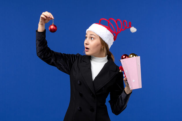 经理前视图年轻女士拿着圣诞树玩具在蓝色的墙上蓝色的情感新年假期人女人职业