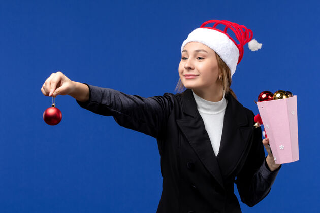 微笑前视图年轻女士拿着树玩具在蓝色的墙上情感新年假期蓝色人观点玩具