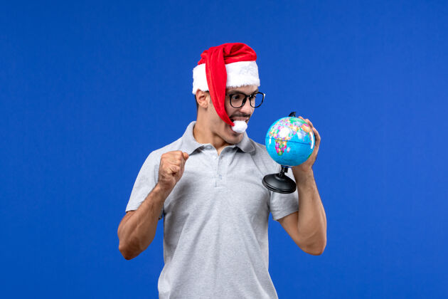 运动正面图年轻的男性手持地球仪在蓝色的墙壁上度假旅行男性人表演地球仪