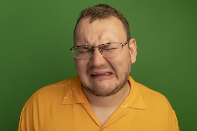 用力一个戴着眼镜 穿着橙色衬衫的男人站在绿色的墙上 痛苦地哭着 脸上带着绝望的表情表情哭泣眼镜