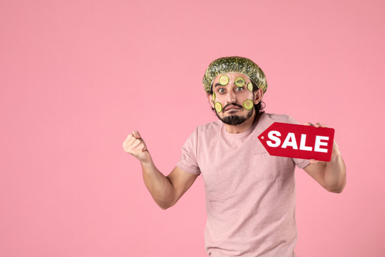 男性正面图：年轻男性 脸上戴着面具 手持粉色背景的销售铭牌持有人视图