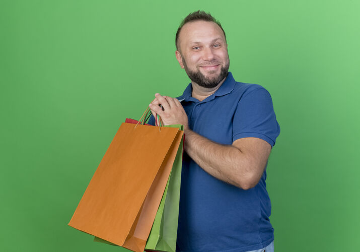 看高兴的成年斯拉夫男子拿着购物袋隔离在绿墙上男人拜托购物