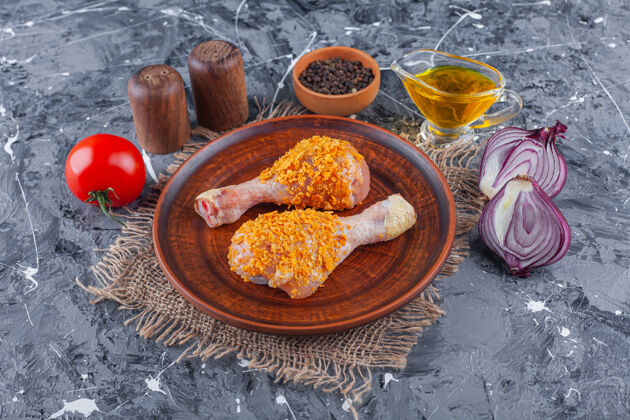 禽类把腌好的鸡腿放在盘子里的麻布上 旁边放着香料和洋葱 放在蓝色的桌子上生的生的美味